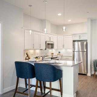 A modern kitchen with a stylish white and stainless steel design, featuring bar stools and wood flooring.
