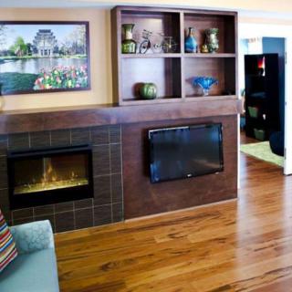 A cozy living room with a fireplace and mounted television, featuring decorative shelves and wood flooring.