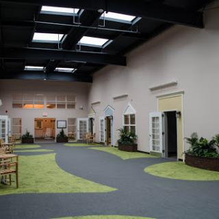 A spacious interior hallway featuring multiple doors, natural lighting from skylights, and a carpeted floor with green accents.
