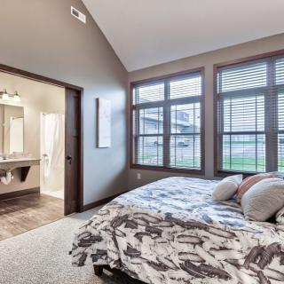 A modern bedroom featuring large windows that allow natural light to fill the space. The room is decorated with neutral colors and a comfortable bed, leading to an adjacent bathroom.