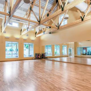 A spacious dance studio with a wooden floor and large mirrors, featuring bright lighting and exposed beams.