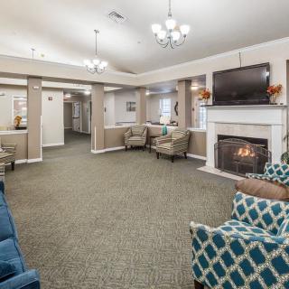 A spacious lounge area with a fireplace, comfortable seating, and a television, illuminated by chandeliers.