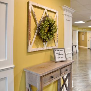 A hallway featuring a rustic table with decorative wall art and a wreath above.