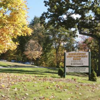 A park sign surrounded by autumn trees and fallen leaves.