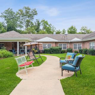 A well-maintained garden with a patio area, featuring comfortable chairs, a swing, and a paved pathway.