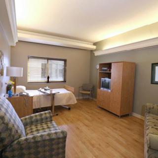 A clean and well-lit hospital room with a patient bed, chairs, and a window.
