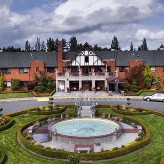 A grand hotel with Tudor-style architecture features a central circular fountain and well-maintained gardens.