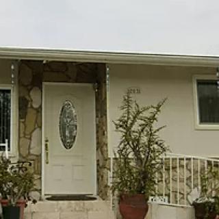 Front view of a house with a white door and potted plants on the porch.