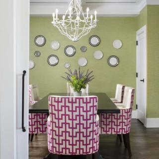 A stylish dining room with green walls adorned with decorative plates, featuring patterned chairs and a central chandelier.