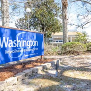 A blue sign for Washington Rehabilitation and Healthcare Center, surrounded by trees and a building in the background.