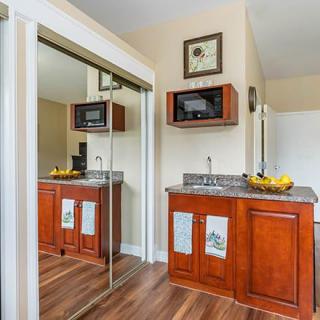 A compact kitchen area featuring wooden cabinets, a wall-mounted microwave, and mirrored doors.