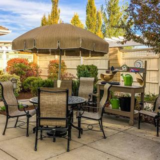 A cozy patio with a table, chairs, and an umbrella surrounded by plants.