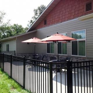A sunny outdoor patio with tables and red umbrellas next to a building, surrounded by a black metal fence.
