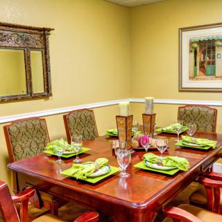 A warmly decorated dining room with a wooden table set for six, featuring green-themed place settings and decorative elements including a mirror and artwork on the walls.