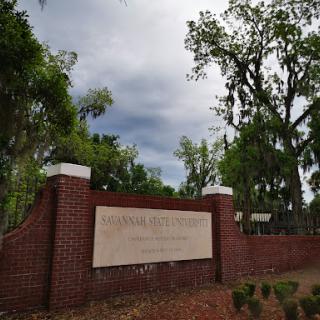 A view of a brick sign at the entrance surrounded by lush greenery under a cloudy sky.