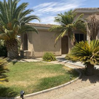 A sunny day view of a house with palm trees and a well-maintained garden.