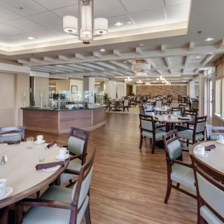 A modern and spacious restaurant dining area with neatly arranged tables and chairs under elegant light fixtures.