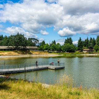 A scenic view of a tranquil lake with a dock, surrounded by trees and under a partly cloudy sky.