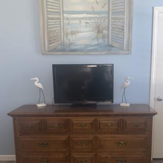 A dresser with a television and bird figurines, topped by a painting of an open window scene.