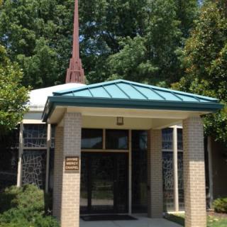 A small church building with a steeple and trees surrounding it.