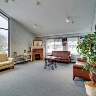 A cozy living room with sofas, a coffee table, and a fireplace, bathed in natural light from large windows.