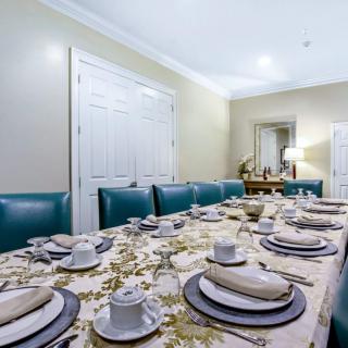 An elegantly set dining table with an ornate tablecloth, fine china, and upholstered chairs in a well-decorated room.