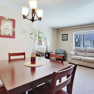 A cozy dining and living area with a wooden table, chairs, and a sofa under natural lighting.