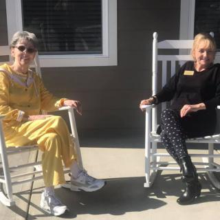 Two people sitting in rocking chairs outside on a sunny day.