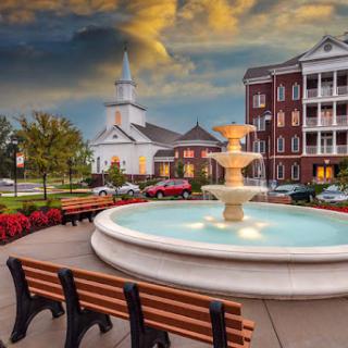 A picturesque park featuring a central fountain surrounded by benches and a charming church in the background.