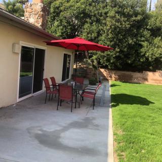 A cozy patio setup with a table and chairs under a red umbrella, situated next to a lush green lawn.