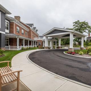 A modern building with a covered entrance and landscaped driveway on a cloudy day.