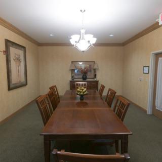 A formal dining room with a long wooden table, surrounded by chairs and lit by a chandelier.