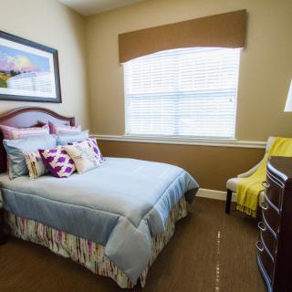 A cozy bedroom with a neatly made bed, decorative pillows, and a large window letting in natural light.