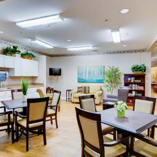 A cozy dining area with neatly arranged tables and chairs, decorated with plants and warm lighting.