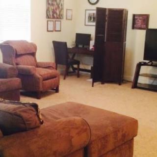 A cozy living room with brown furniture, featuring a sofa, armchair, TV, and an office desk.