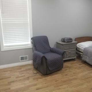 A minimalist bedroom with a gray armchair, bed, and nightstand on a wooden floor.