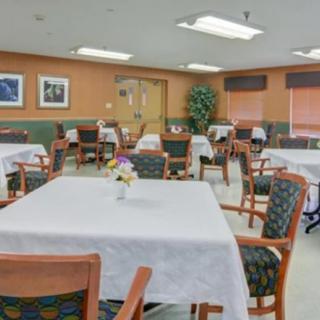 An empty dining room with neatly arranged tables and chairs, covered with white tablecloths.