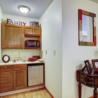 A small kitchen area with wooden cabinets and a countertop, featuring decorative items and a mirror on the adjacent wall.