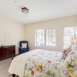 A bright and cozy bedroom with floral bedding, a dresser, and large windows.