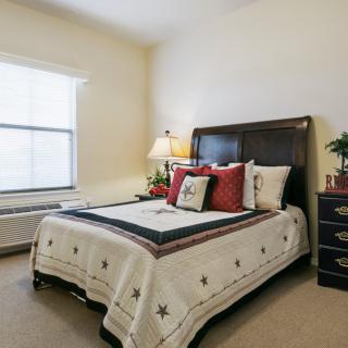 A cozy and well-decorated bedroom featuring a bed with patterned bedding, a bedside lamp, and a window allowing natural light in.