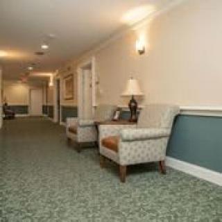 A hallway with armchairs and a lamp, featuring carpeted flooring and wall sconces.