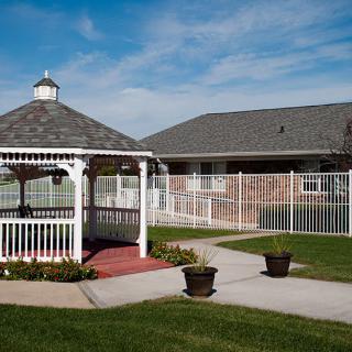 A peaceful outdoor area featuring a white gazebo with a brick pathway and green lawn, set against a clear blue sky.