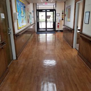 A view of a brightly lit hallway with wooden floors and decorative artwork on the walls, leading towards double doors.