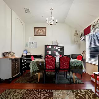 A well-decorated dining room with a table, chairs, and bookshelf, featuring a chandelier and large window for natural light.
