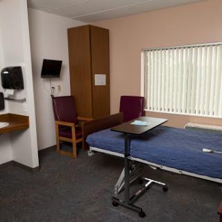A clean and simple hospital room equipped with a bed, chairs, and essential medical facilities.