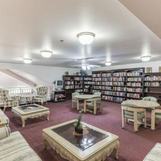 A cozy library featuring bookshelves filled with books, surrounded by comfortable seating and tables on a carpeted floor.
