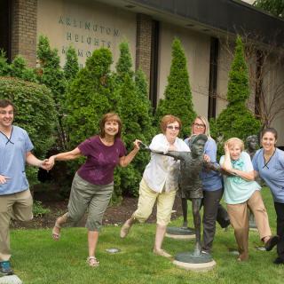 A group of people posing playfully with statues outside a building.