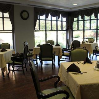 A cozy dining room with neatly arranged tables and chairs, illuminated by natural light from large windows.