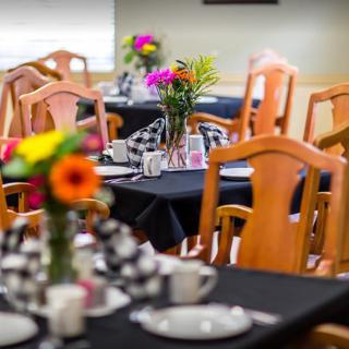 A cozy dining area with wooden chairs and tables adorned with colorful flowers and neatly set tableware.