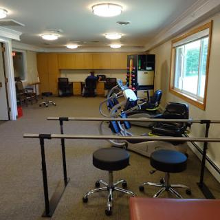 A spacious rehabilitation therapy room equipped with exercise equipment and a parallel bar for patient use.